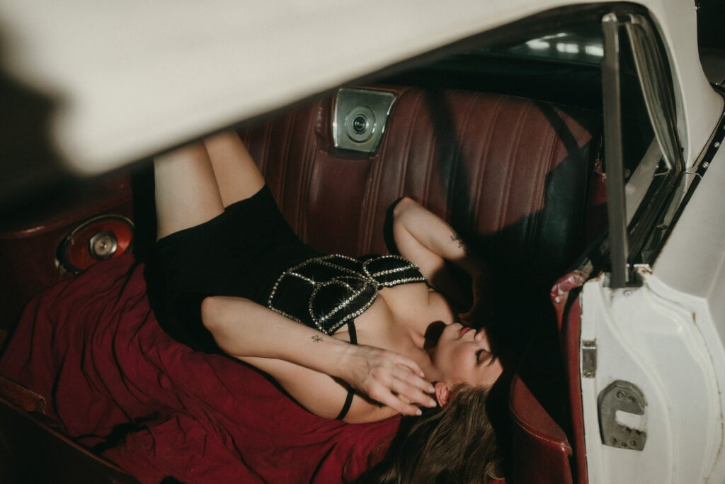 woman in a black out fit lying on the backseat of a vintage white car.